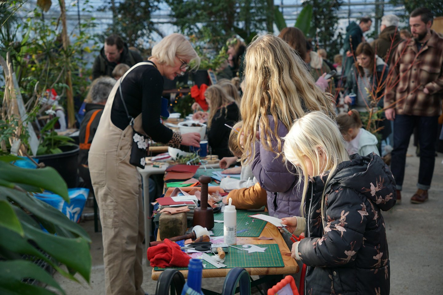 Diverse people craft together at a long table in a greenhouse.