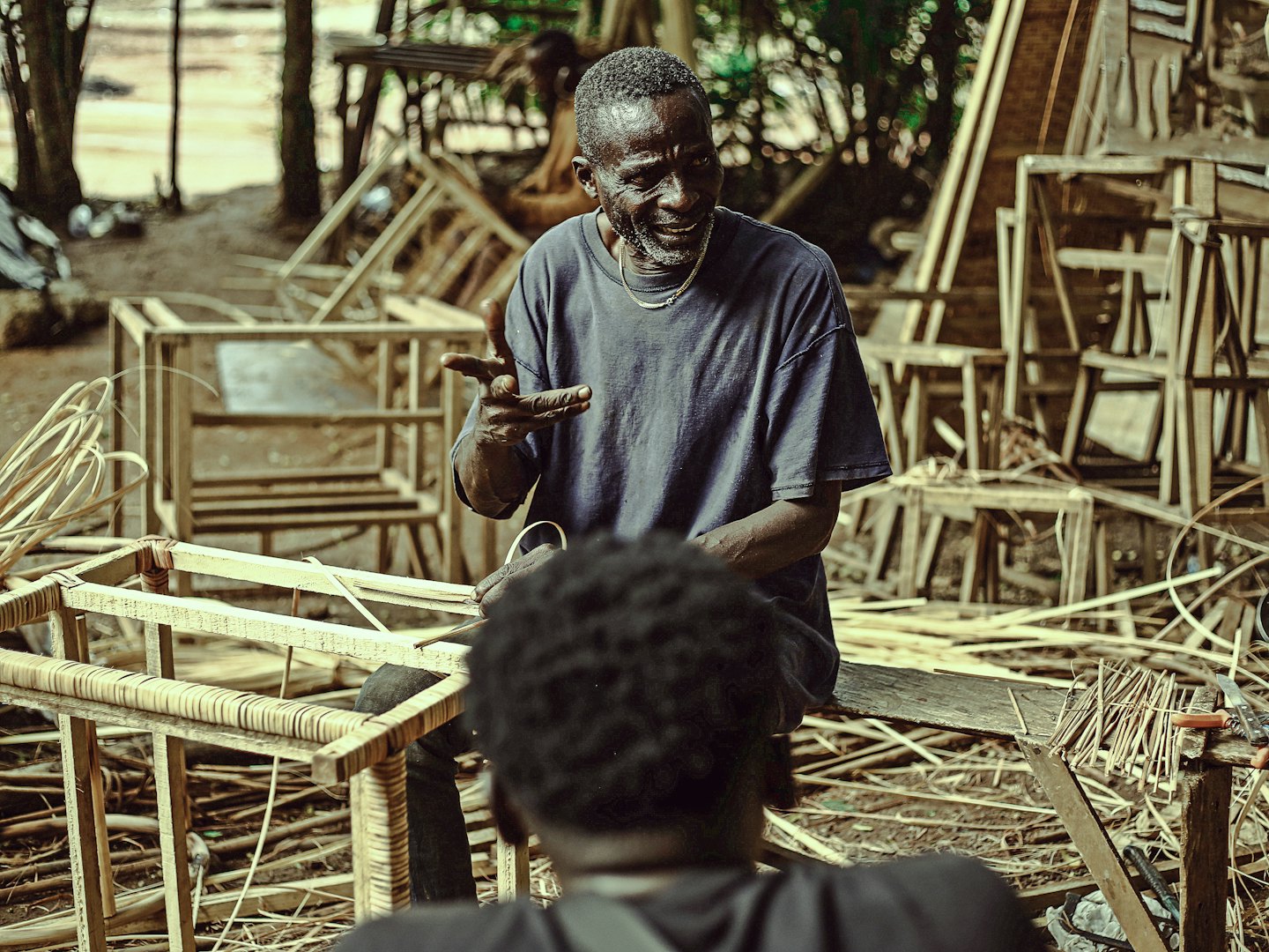 Craftsman teaching student in an outdoor workshop.
